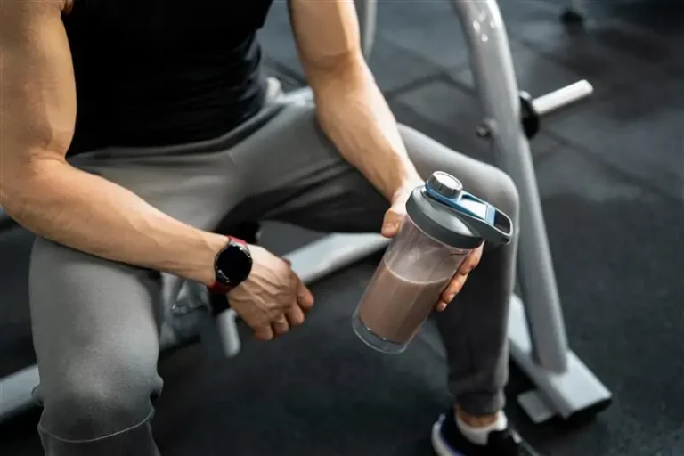 Homem sentado na academia segurando um shaker com bebida suplemento de proteína após o treino