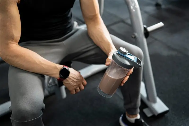 Homem sentado na academia segurando um shaker com bebida suplemento de proteína após o treino